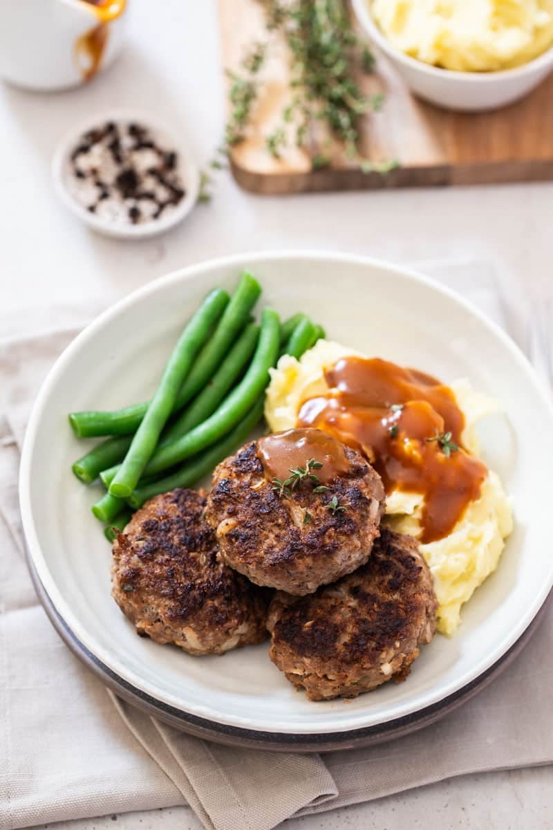 a plate of rissoles and vegetables on a table set with napkins and a wooden board.