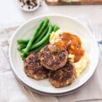 rissoles arranged on a plate with mashed potato, vegetables and gravy.