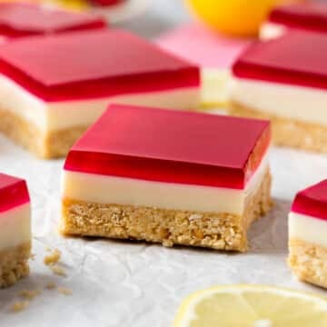 a piece of jelly slice on a table. It has a crumbly biscuit base and a layer of red jelly on top.