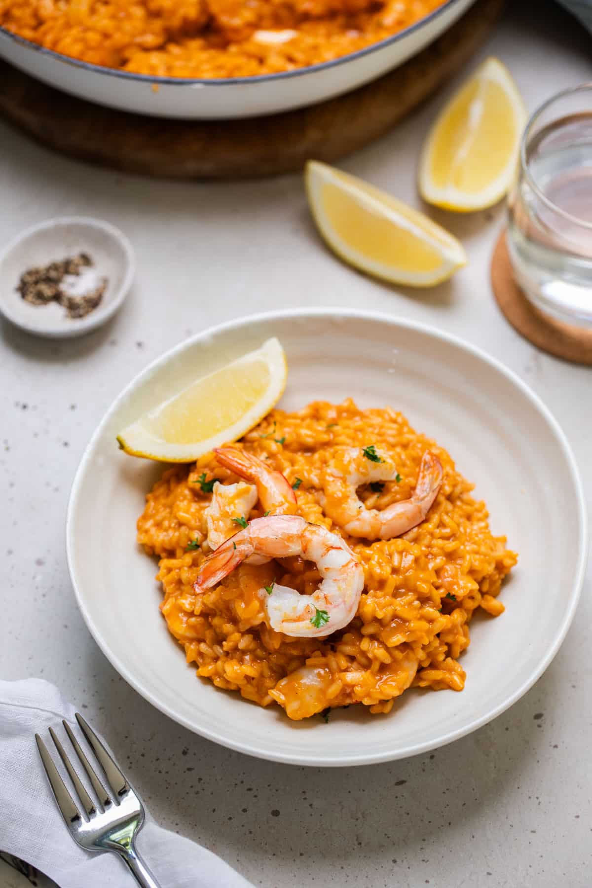 a bowl of risotto topped with prawns and a wedge of lemon.