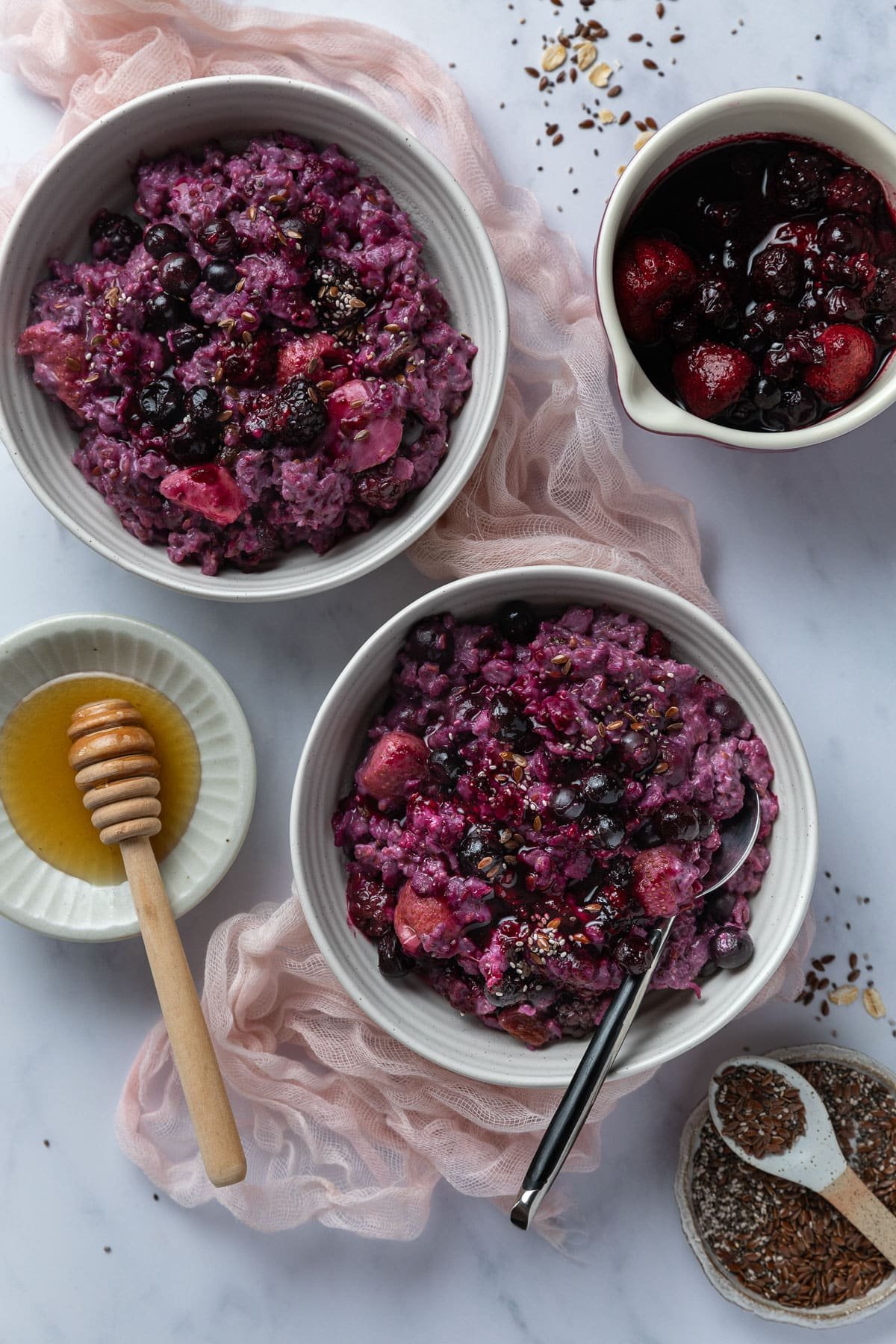 bowls of berry porridge arranged on a table with honey.