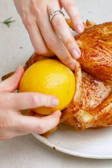 a whole lemon being inserted inside the cavity of a chicken.
