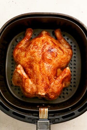 a whole chicken, lying breast-side down in an air fryer basket.