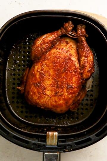 a finished roast chicken, in an air fryer basket.