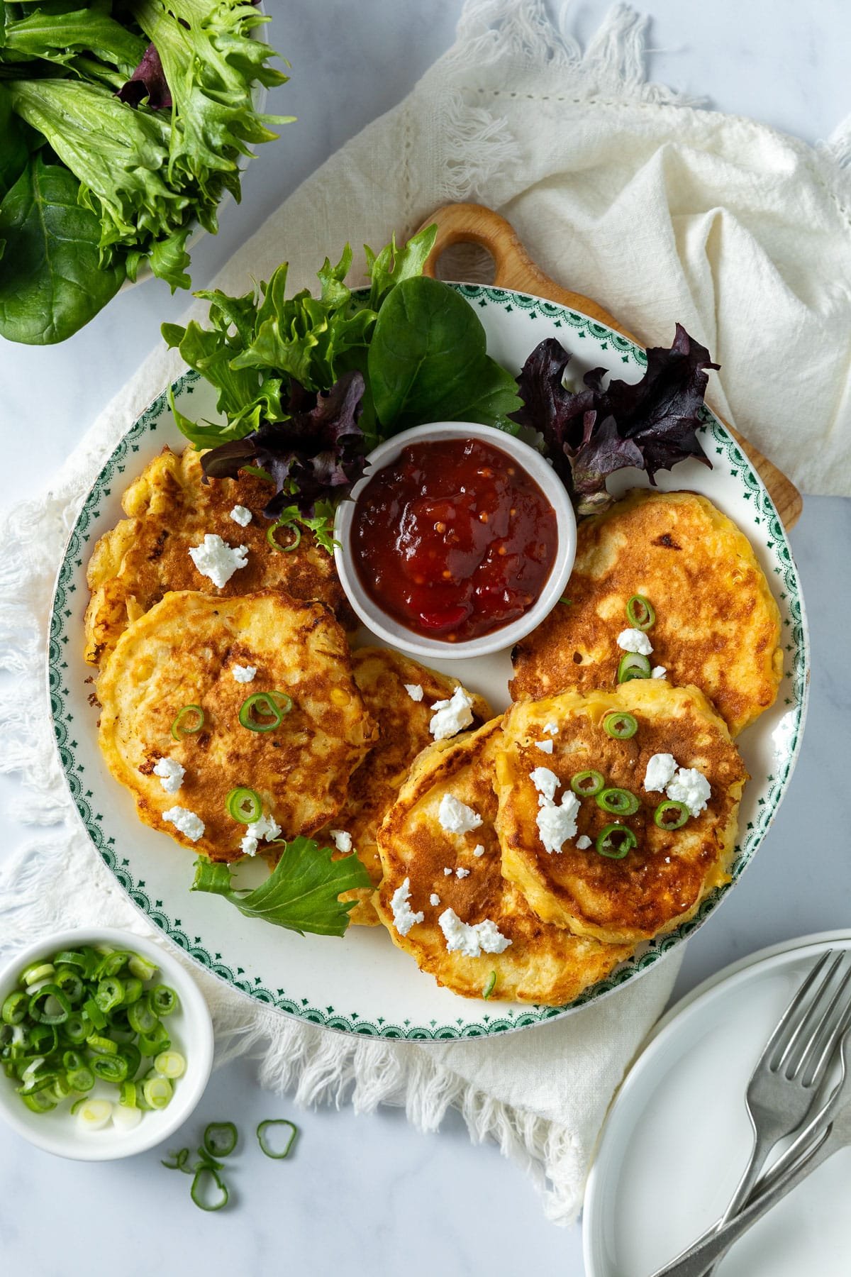 creamed corn fritters on a plate, with salad, tomato sauce and crumbled feta.