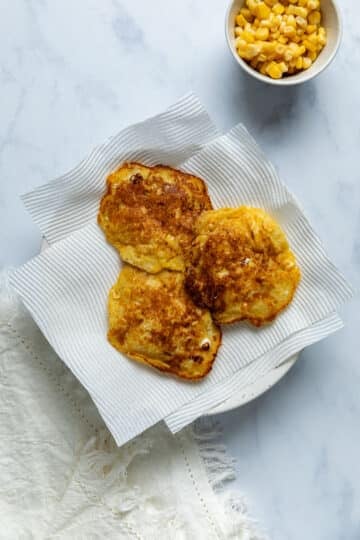 finished corn fritters, resting on a plate lined with paper towel.