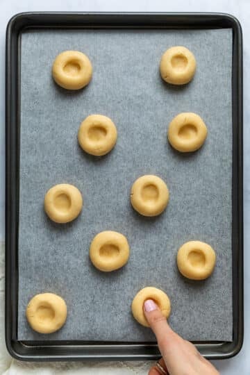 a hand pressing holes into the centre of the dough balls on a baking tray.