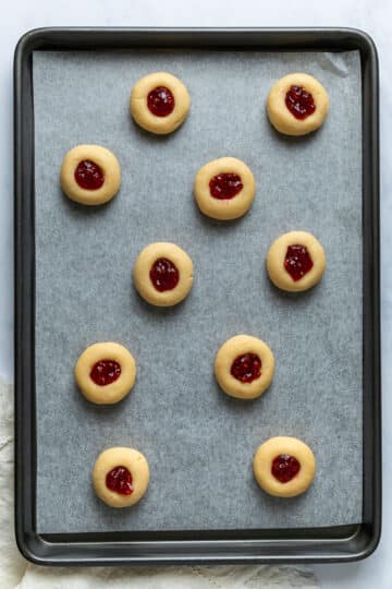 prepared biscuits filled with jam, arranged on a lined baking tray.