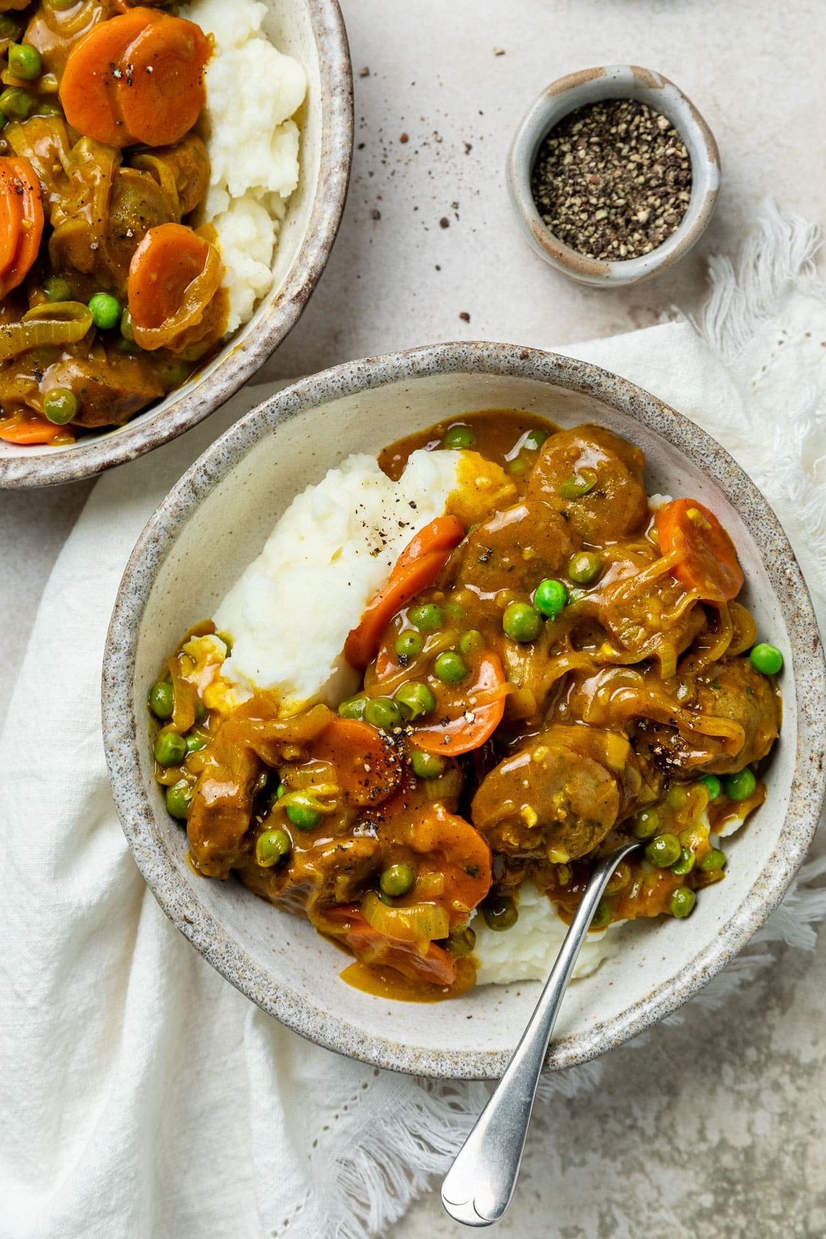 a bowl of curried sausages atop mashed potatoes, on a table.