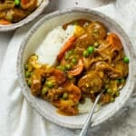 a bowl of curried sausages with vegetables and mashed potato.