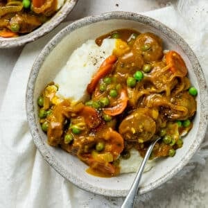 a bowl of curried sausages with vegetables and mashed potato.