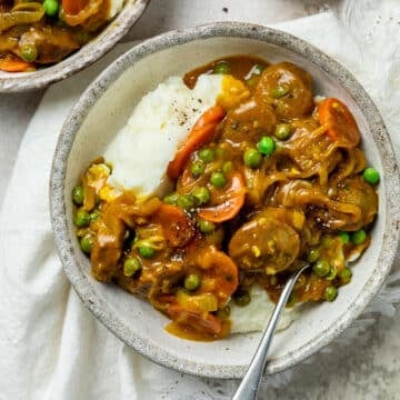 a bowl of curried sausages with vegetables and mashed potato.