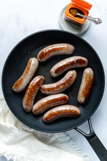 whole, cooked sausages in a frying pan.