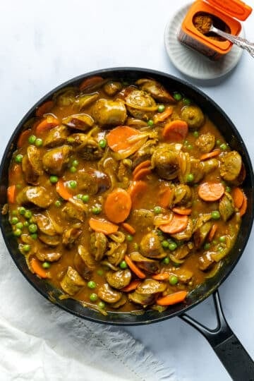 finished curried sausages in a large frying pan. There is an opened tin of Keens curry powder to the side.