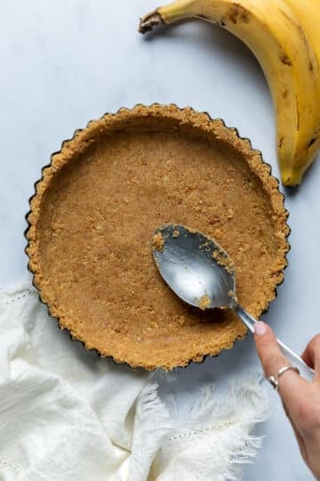 a biscuit base being pressed into a pie dish with a spoon.