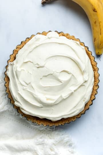 whipped cream layered over the top of banoffee pie in a pie tin.