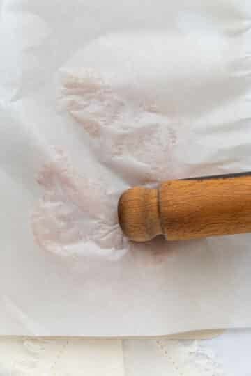 a rolling pin flattening chicken breast which is covered in baking paper.