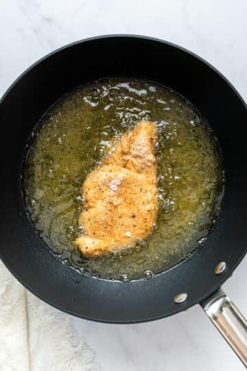 chicken frying in a pan with oil.
