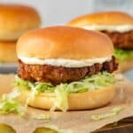 a burger with crispy chicken, shredded lettuce and mayo on a board.