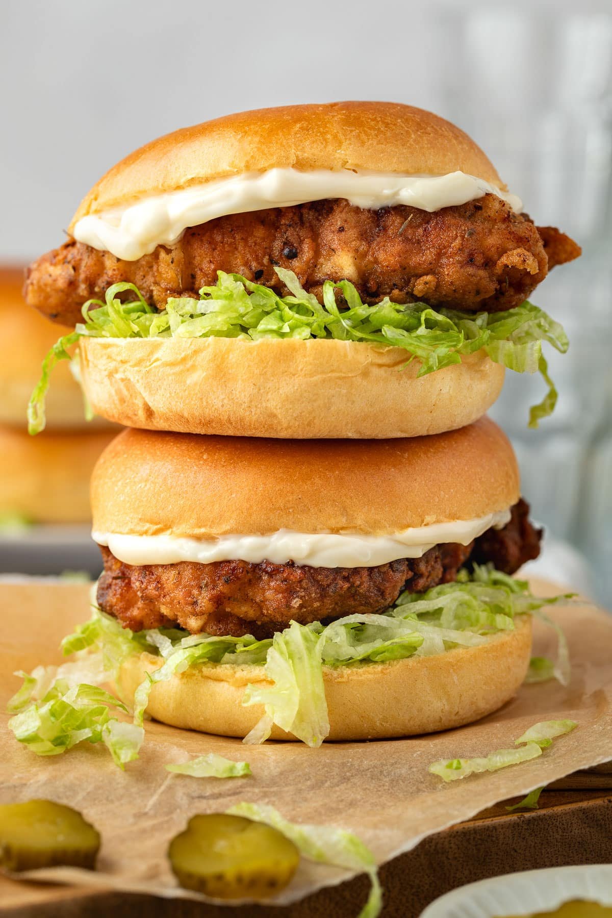 two crispy chicken burgers stacked on a wooden board.