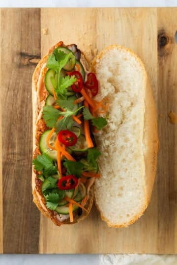 a sliced baguette filled with sliced pork, pickled vegetables, herbs and chilli.