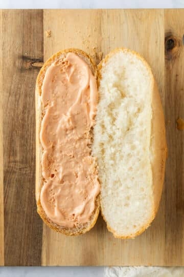 a Vietnamese baguette on a board. Chilli mayo is spread over one side.