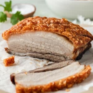 pork belly with crispy skin on a board, with slices of pork.