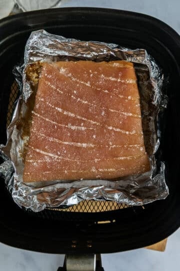 pork belly in an air fryer basket. The salt has been removed from the skin.