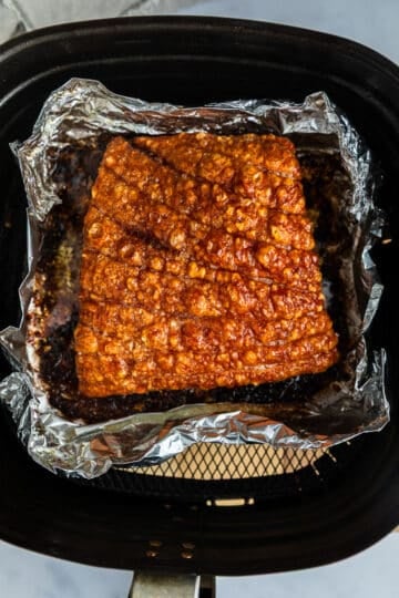 finished roast pork belly in an air fryer basket. The skin is puffed and crispy.