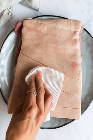 a hand using paper towel to dry pork belly skin.