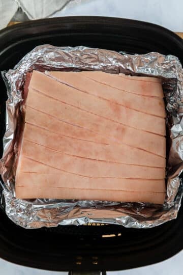 pork belly placed in a foil tray, sitting in an air fryer basket.