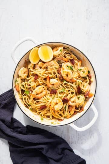 finished pasta in a pan with lemon wedges.