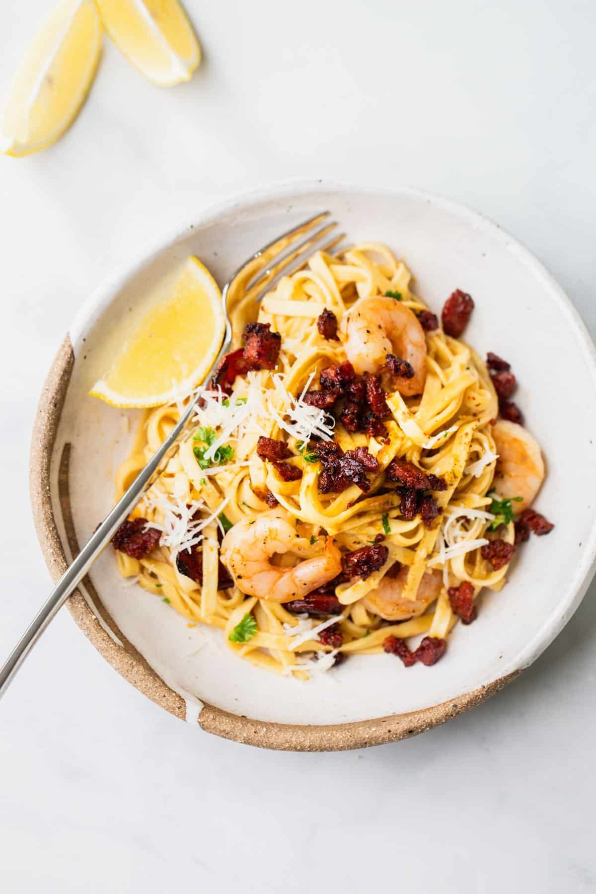 a bowl of prawn and chorizo pasta with a lemon wedge.