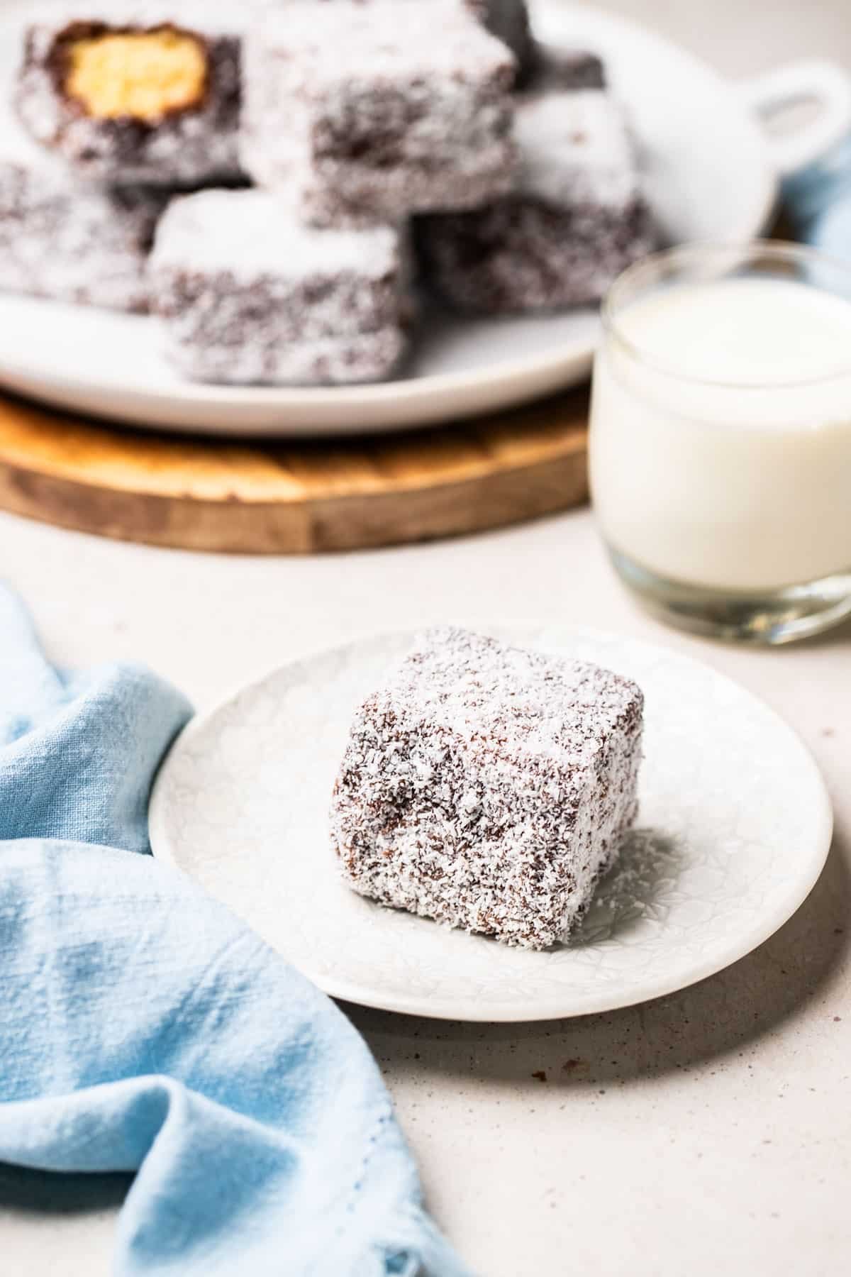 a chocolate lamington coated in coconut on a plate.