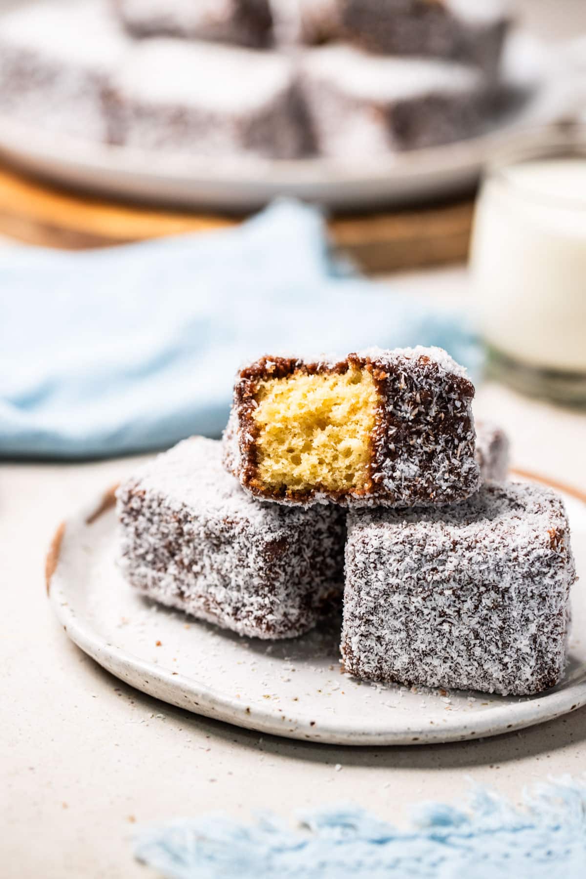 a plate of lamingtons. One has a bite missing, showing the cake underneath the chocolate and coconut layer.
