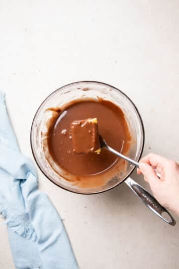 a spoon holding a piece of cake being placed into chocolate glaze.