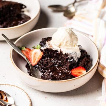 a bowl of chocolate pudding and sauce, topped with ice cream and strawberries.