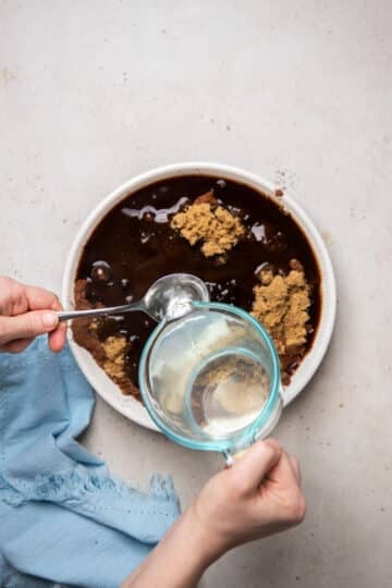 water in a jug, being poured onto the top of a chocolate pudding batter. A spoon is being used to slow the flow of water.